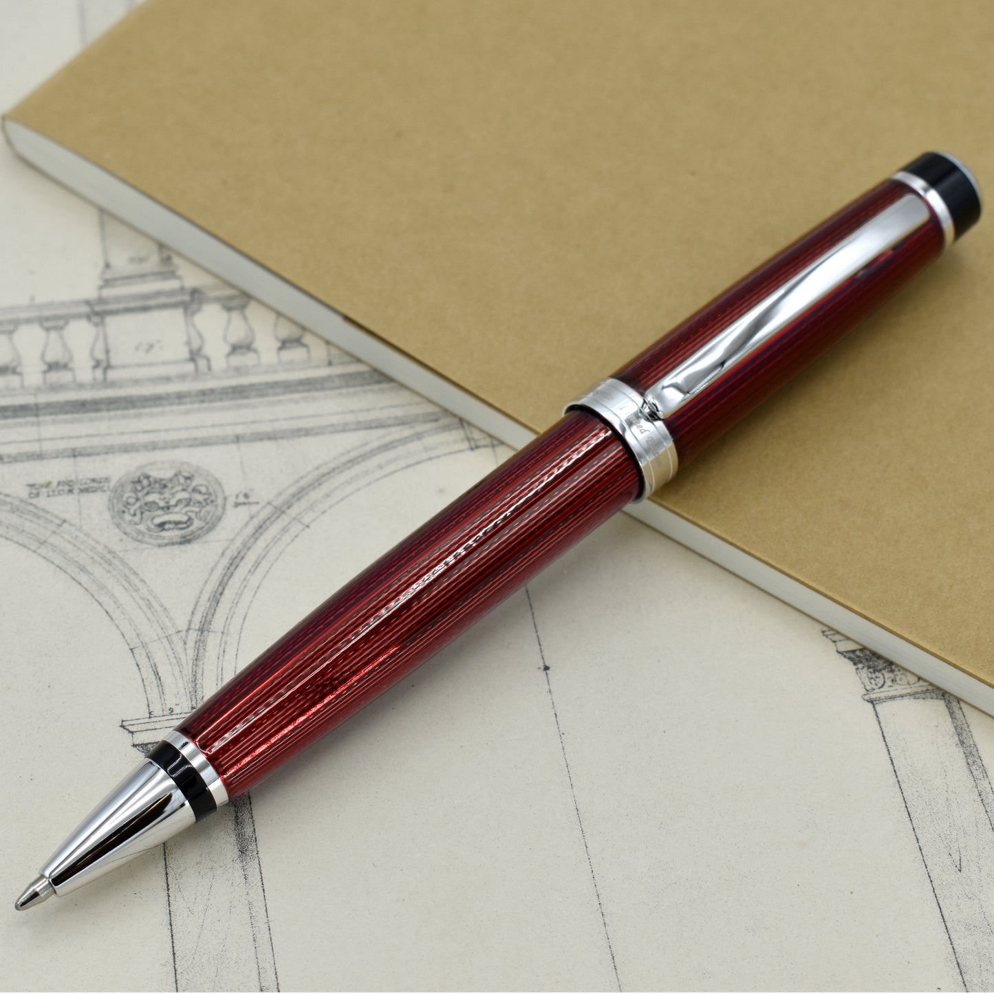 Incognito Burgundy B Ballpoint pen with antique architectural sketches and a notebook