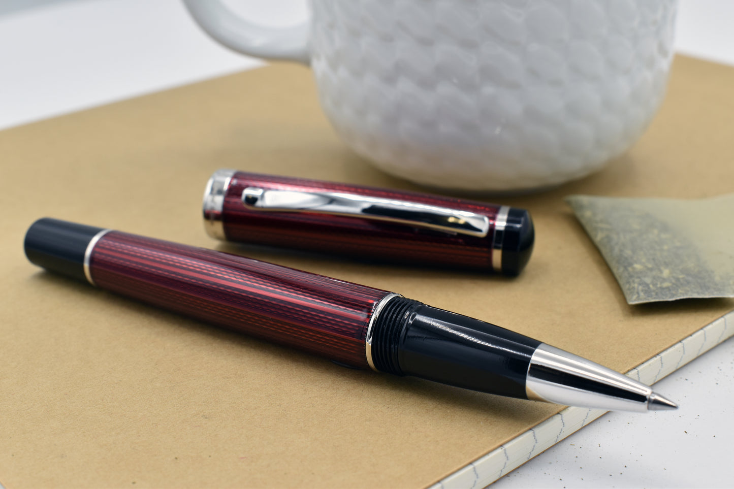 Incognito Burgundy R-1 Rollerball pen next to a mug