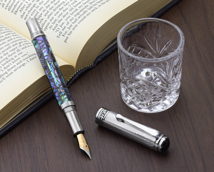 Maestro Paua Abalone Chrome F Fountain pen with a book and glass cup
