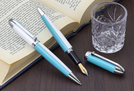 Set of Visionary Sky Blue/White B ballpoint and Visionary Sky Blue/White FM fountain pens propped against a book.