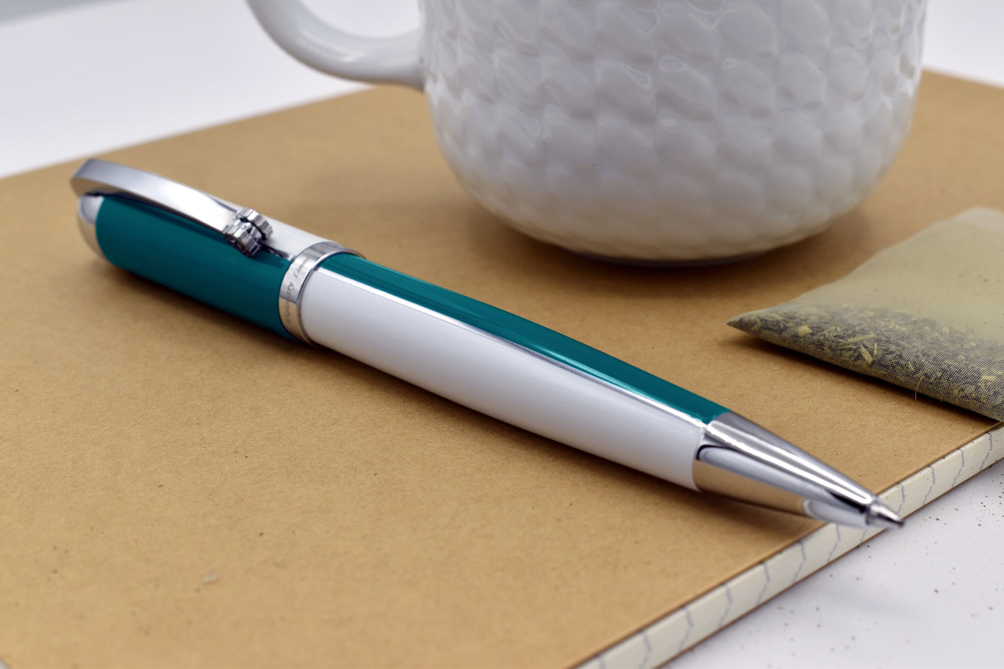 Visionary Teal Green/White B Ballpoint pen next to a mug