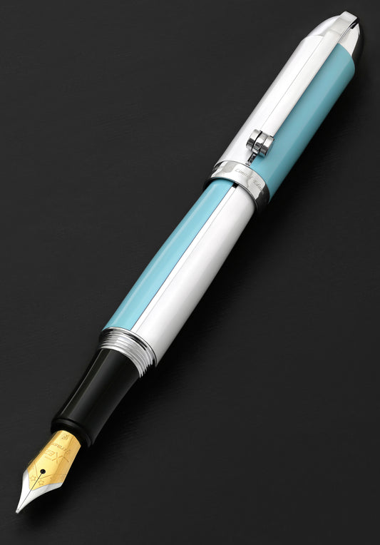 Xezo - The Visionary Sky Blue/White F fountain pen laying on a backdrop, with the cap posted on the end of the barrel